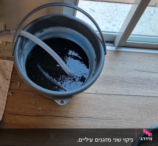 דלי עם צינור ניקוז ממזגן מלא במים כהים